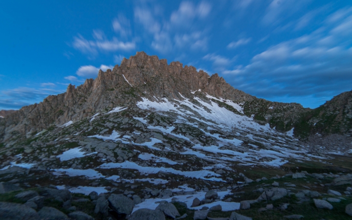 Snow dots a rocky mountain under a blue sky.
